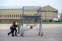 Aircraft ground equipment technicians working for the 501st Combat Support Wing guide a maintenance stand