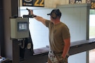 Man in USAMU shooting uniform firing pistol on outdoor pistol range.