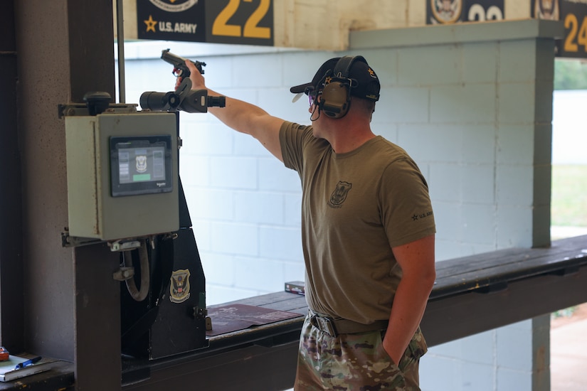 Man in USAMU shooting uniform firing pistol on outdoor pistol range.