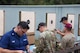 Multiple men in shooting uniforms reviewing targets on outdoor pistol range.