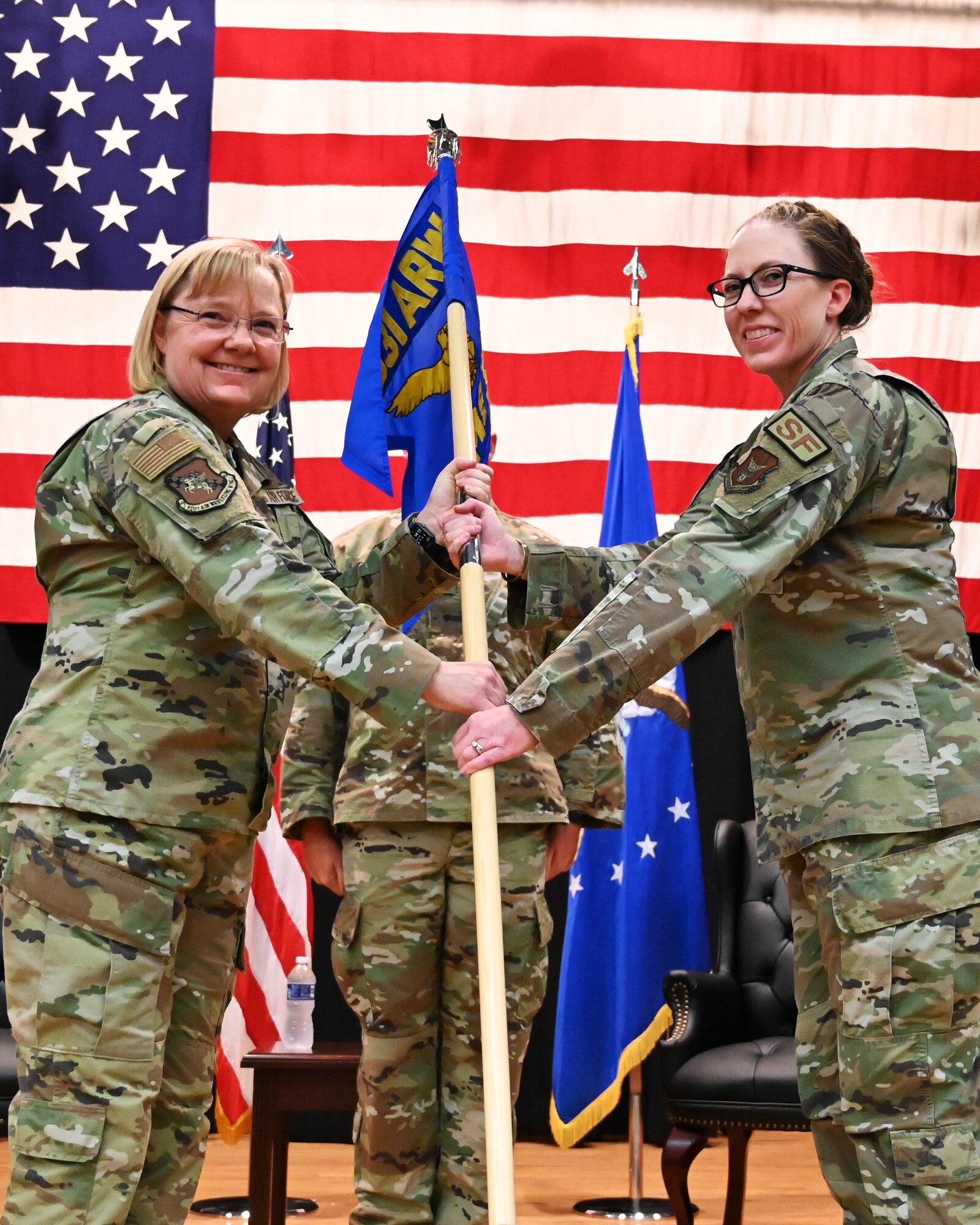 (From left to right) Col. Cynthia Welch, 931st Air Refueling Wing commander, hands the guideon to Lt. Col. Vanessa Schoon, incoming 931st Air Refueling Wing commander. They are in front of an American flag.