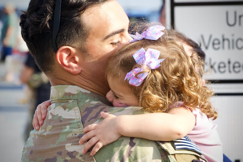 A guardsman lifts a child into a tight embrace during the day.