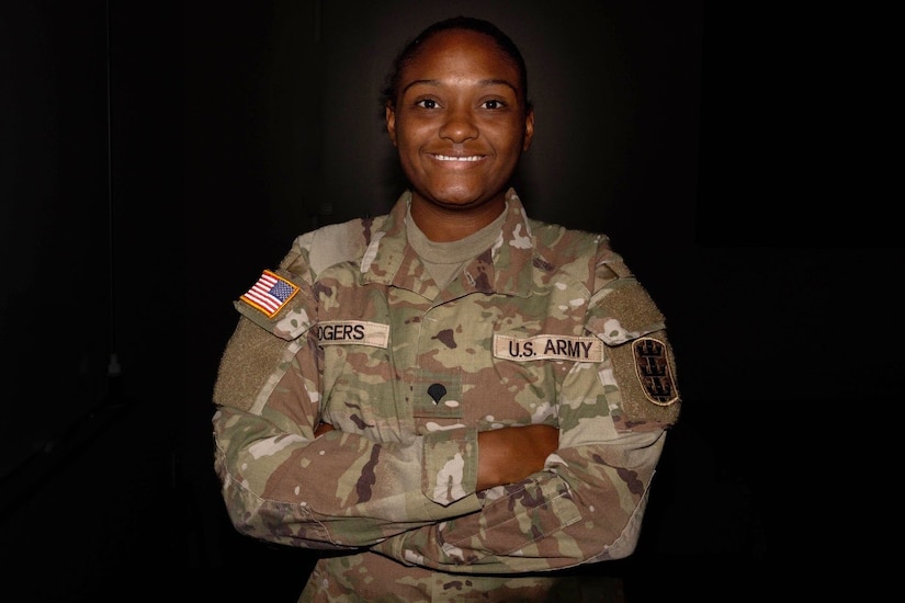 A soldier stands with arms folded and smiles for a photo.