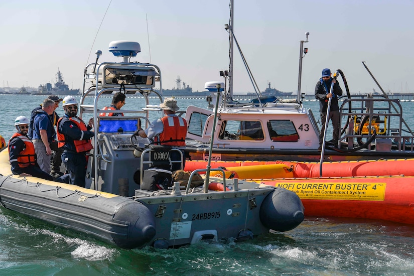 Sailors stand on boats and rubber rafts in a harbor.