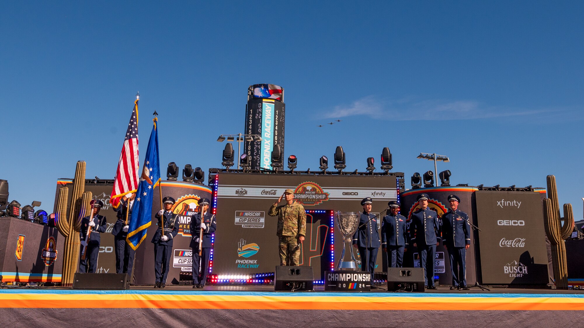 Three A-10C Thunderbolt II’s assigned to the Tucson Air National Guard, honor guardsmen assigned to the 56th Fighter Wing (left), the Air Force Singing Sergeants (right), and U.S. Air Force Air National Guard Major Nathan Tarr (center), 161st Air Refueling Wing chaplain, perform the opening ceremony during the NASCAR Championship pre-race events November 10, 2024, at Phoenix Raceway in Avondale, Arizona.
