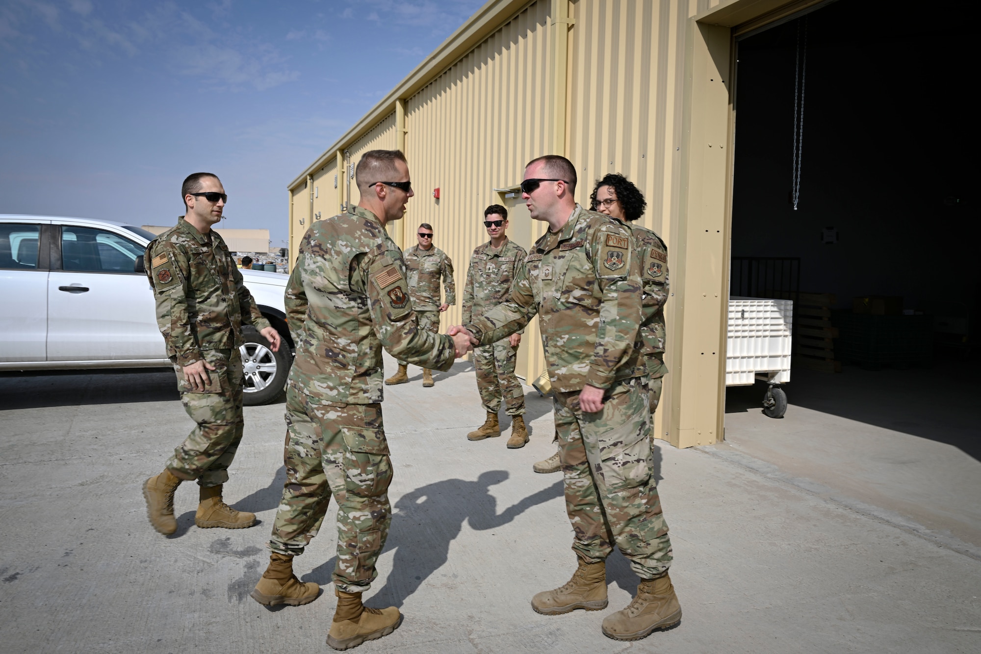 Two military members shake hands during a visit to a work center.