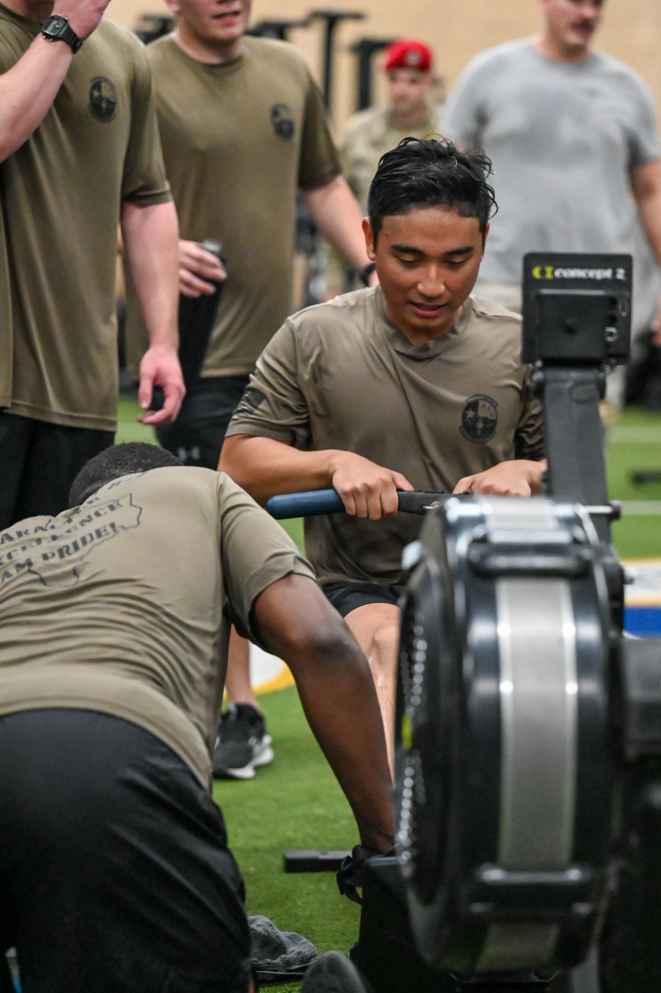 An AFROTC cadet exercises on a row machine as his teammates cheer him on