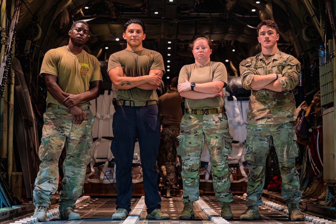 Four uniformed service members stand shoulder to shoulder in the cargo bay of a military aircraft.