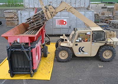A forklift is used to place wood pallets into a shredder.