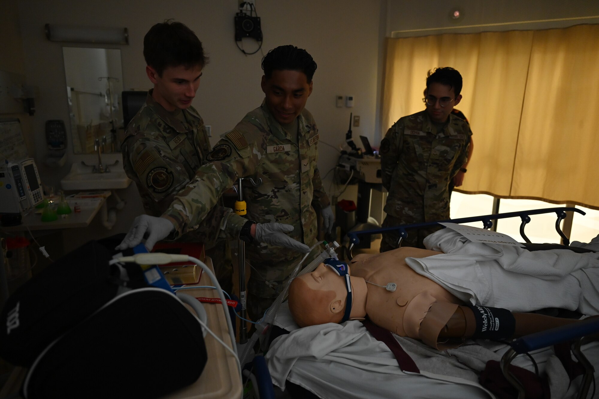 Three Airmen stand around a mannequin looking for clues. 
One Airman touching the defibrillator.