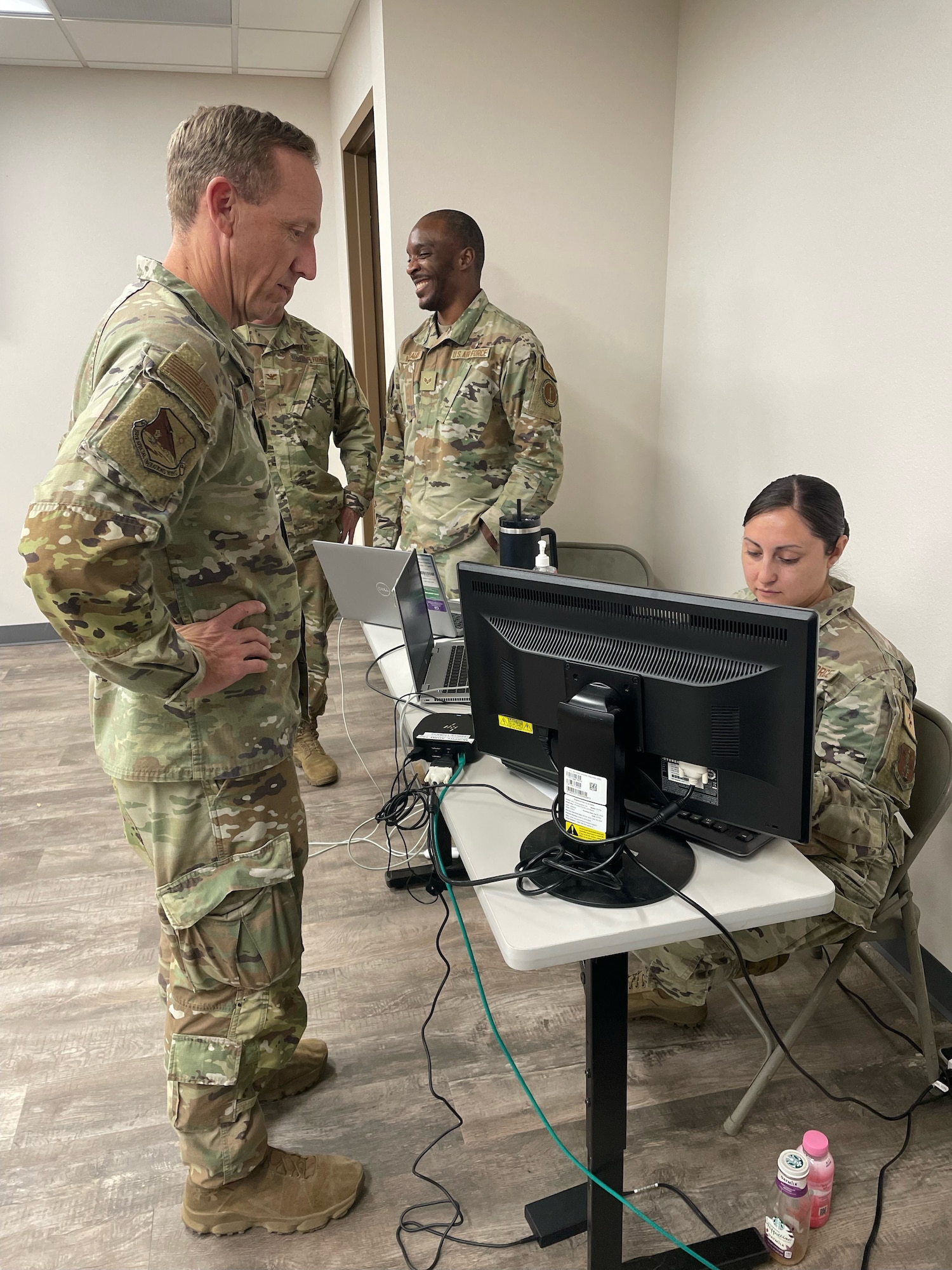 A man in uniform stands in front of a desk with a computer operator behind the desk.