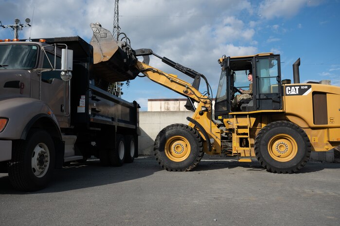 A U.S. Air Force Airman, assigned to the 35th Civil Engineer Squadron, unloads gravel into a dump truck during the Snow Rodeo