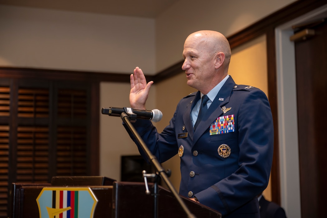 The base commander raises his hand to a crowd of attendees to deliver the honorary commander oath