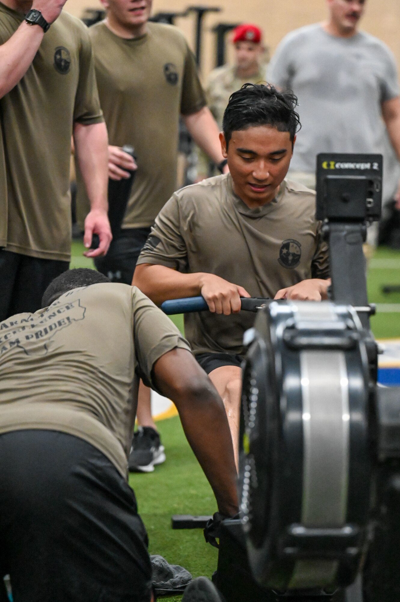 An AFROTC cadet exercises on a row machine as his teammates cheer him on