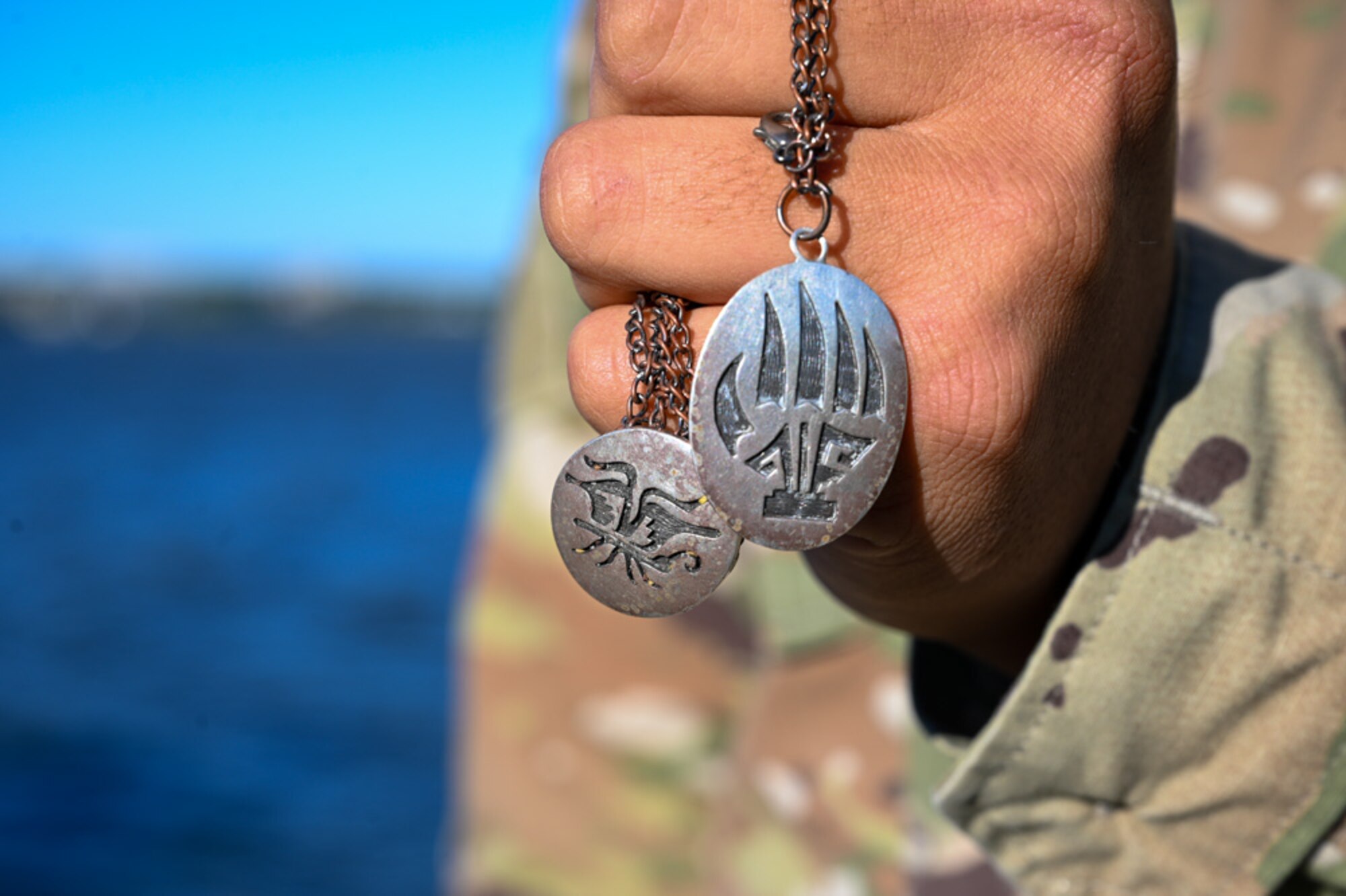 U.S. Air Force Airman 1st Class Isaiah “Dovaaa” Herder holds his Hopi clan’s symbols, Talasi and Butterfly Clan (Left) and the Badger Clan, etched on a chain at the waterfront trail on Joint Base Anacostia-Bolling, Washington, D.C., Oct. 30, 2024. These clans are matrilineal kinship clans in the Hopi tradition. (U.S. Air Force photo by Airman 1st Class Shanel Toussaint)
