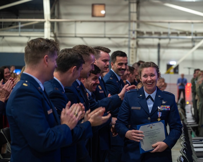 U.S. Air Force decoration recipient walks back to her seat after receiving the Silver Star during a ceremony. Fellow decoration recipients clap and congratulate her.