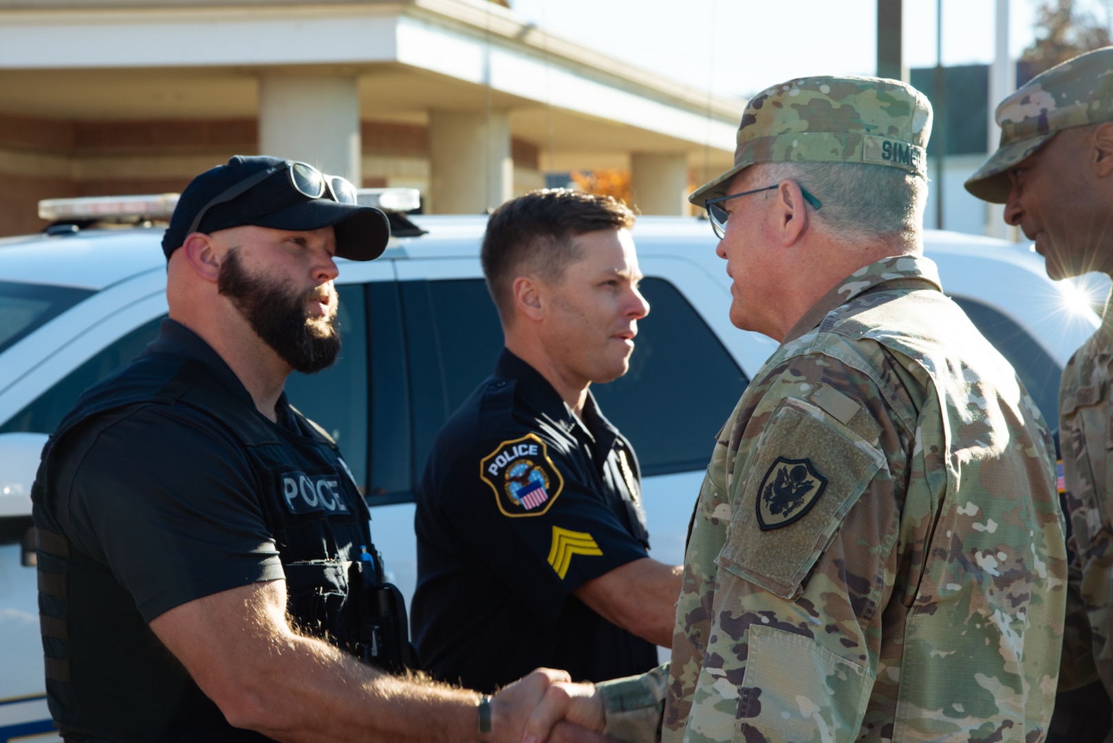 A man in a camouflage military uniform shakes a police officer's hand.