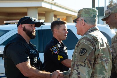 A man in a camouflage military uniform shakes a police officer's hand.
