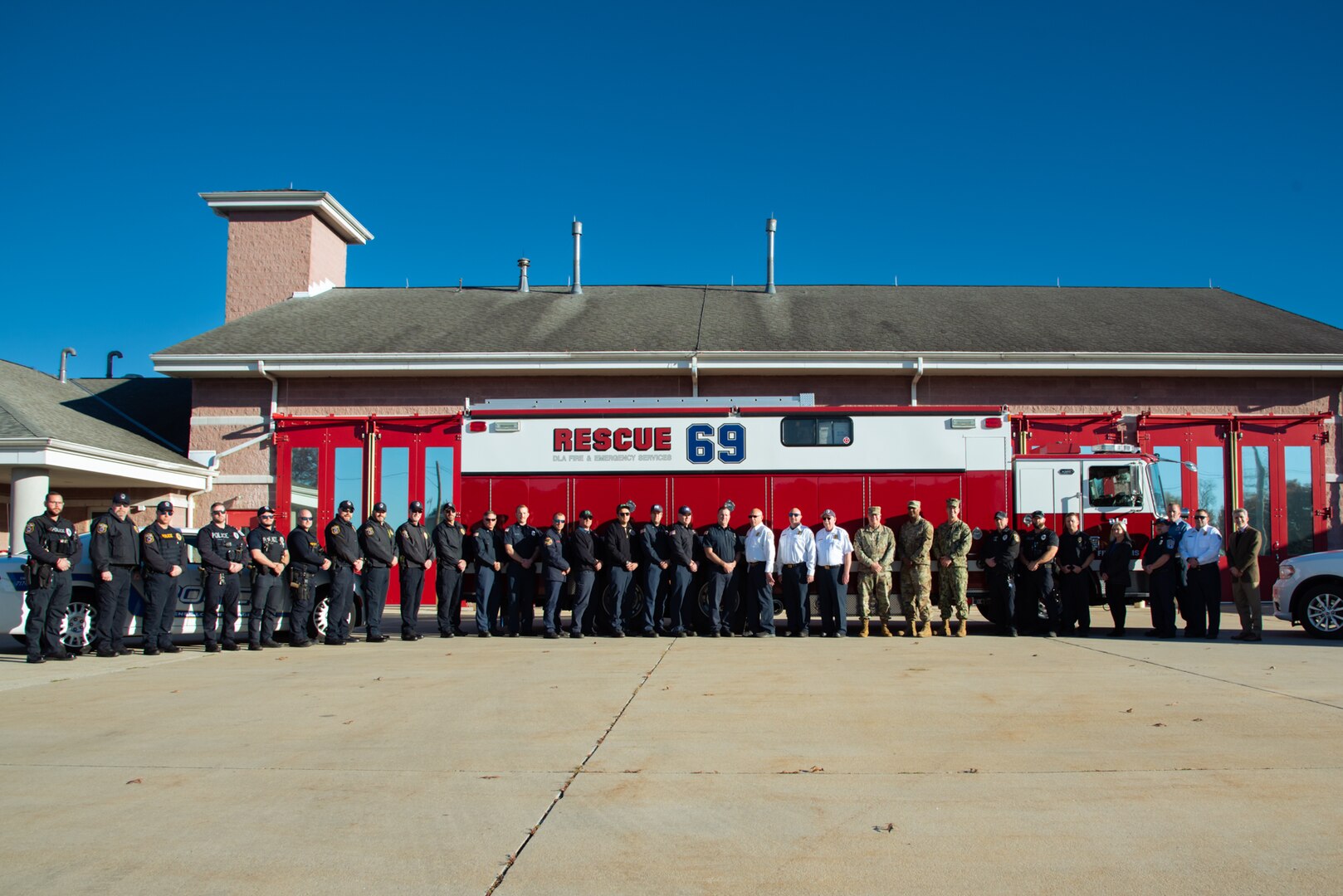 A large group of people stand outside in front of a fire truck that says "Rescue 69" on the side of it.