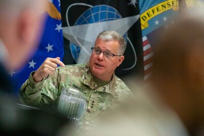 A man in a camouflage military uniform speaks to a group of people.