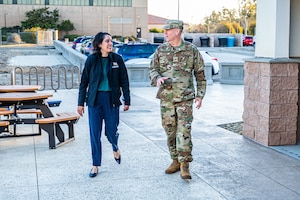 A woman and man walk side by side while talking at the entrance of a building.