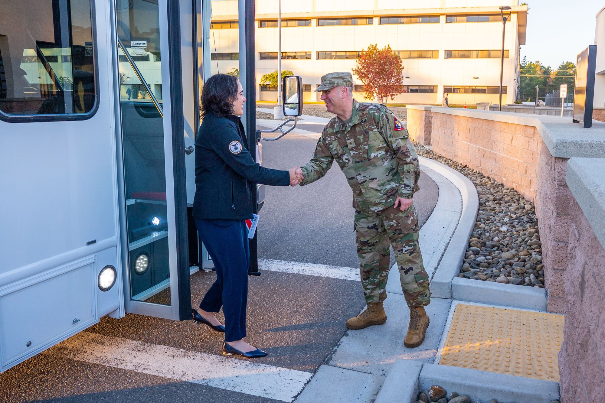 A woman and man shakes hands when greeting each other outside a building.