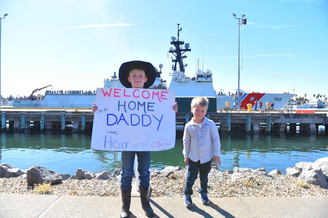 Harper and Henry Helsabeck hold up a sign to welcome home their dad, Lt. Cmdr. Jason Helsabeck, operations officer, Coast Guard Cutter Stratton (WMSL-752), home to Alameda, Calif., Nov. 4, 2024. The Stratton's crew returned home from a months-long Bering Sea Patrol where the crew conducted fisheries law enforcement to protect living marine resources. (U.S. Coast Guard photo by Chief Petty Officer Levi Read/released)