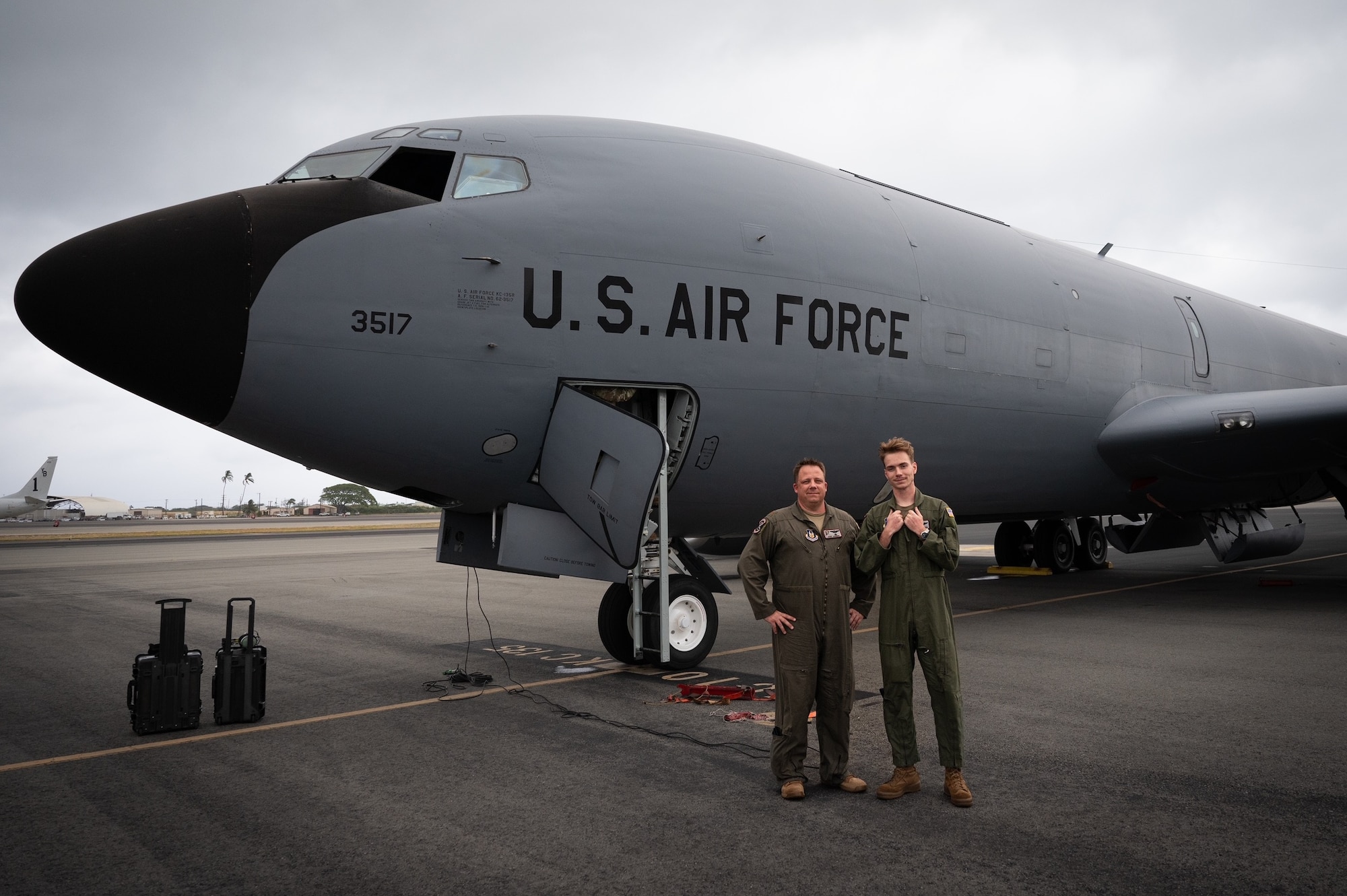 Two men stand in front of a military aircraft.