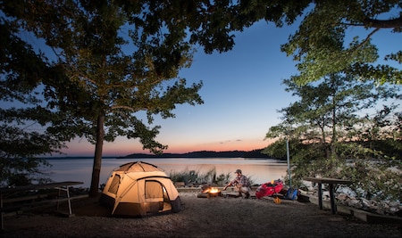 Image of a camping scene at dusk at North Bend Park at Kerr Reservoir with a campfire and tent.