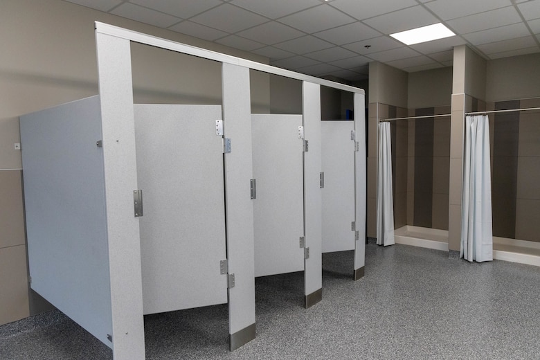 Grey bathroom stalls sit with two shower stalls to the right.