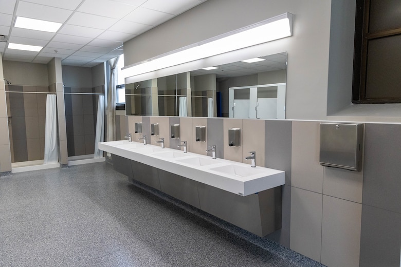 Shower stalls sit to the left with six bathroom sinks and a long mirror in the foreground.
