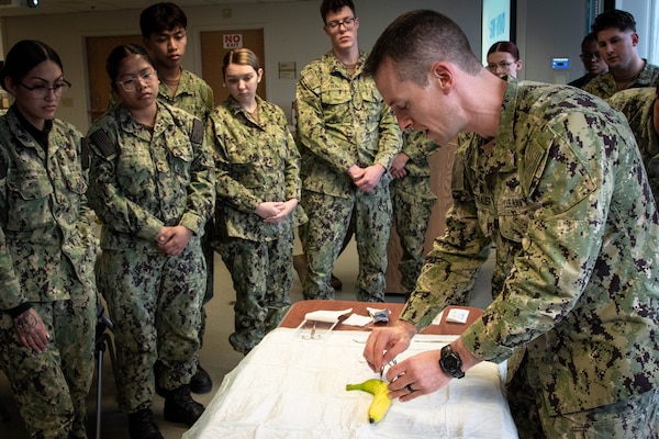 Lt. Cmdr. Jake Wittenauer, DSc- PA-C, Deputy Director of Naval Health Clinic Cherry Point’s Medical Services, right, uses a banana to demonstrate proper suturing to Corpsmen serving aboard Naval Health Clinic Cherry Point on Friday, November 15.  Wittenauer’s demonstration was part of a class teaching the Corpsmen how to properly suture a wound closed utilizing bananas their thick and easy-to-pierce skin and the ability to distinguish the skin from the fruit.