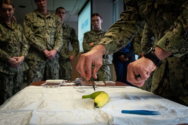 Lt. Cmdr. Jake Wittenauer, DSc- PA-C, Deputy Director of Naval Health Clinic Cherry Point’s Medical Services, right, uses a banana to demonstrate proper suturing to Corpsmen serving aboard Naval Health Clinic Cherry Point on Friday, November 15.  Wittenauer’s demonstration was part of a class teaching the Corpsmen how to properly suture a wound closed utilizing bananas their thick and easy-to-pierce skin and the ability to distinguish the skin from the fruit.