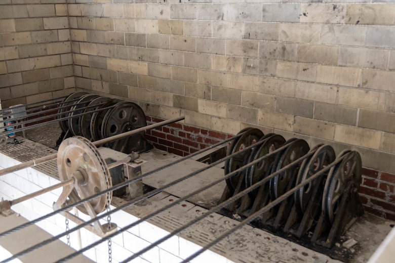 Dark brown mechanical pieces sit in front of a grey cinder block wall.