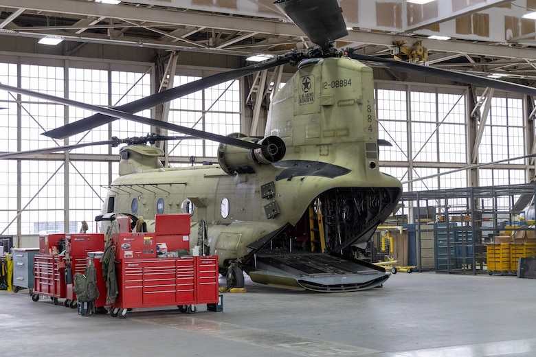 A grey helicopter sits next to red tool storage carts with windows in the background.