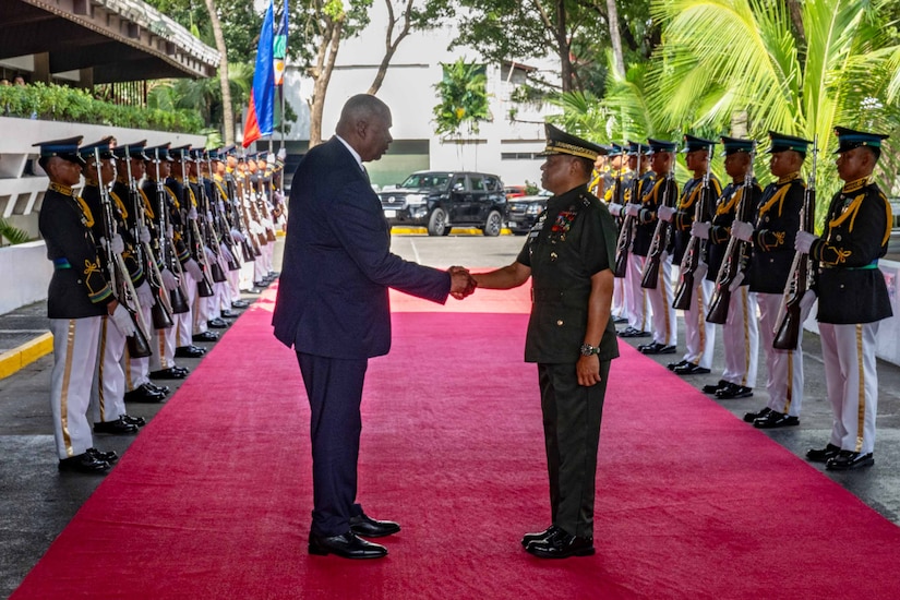 A man in civilian attire shakes hands with a man in a foreign military uniform.