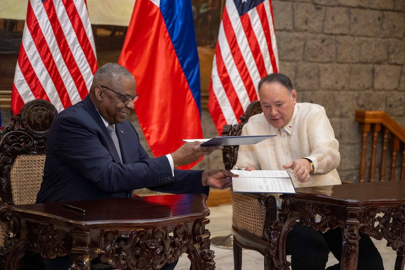 Two men in civilian attire hold document folders.