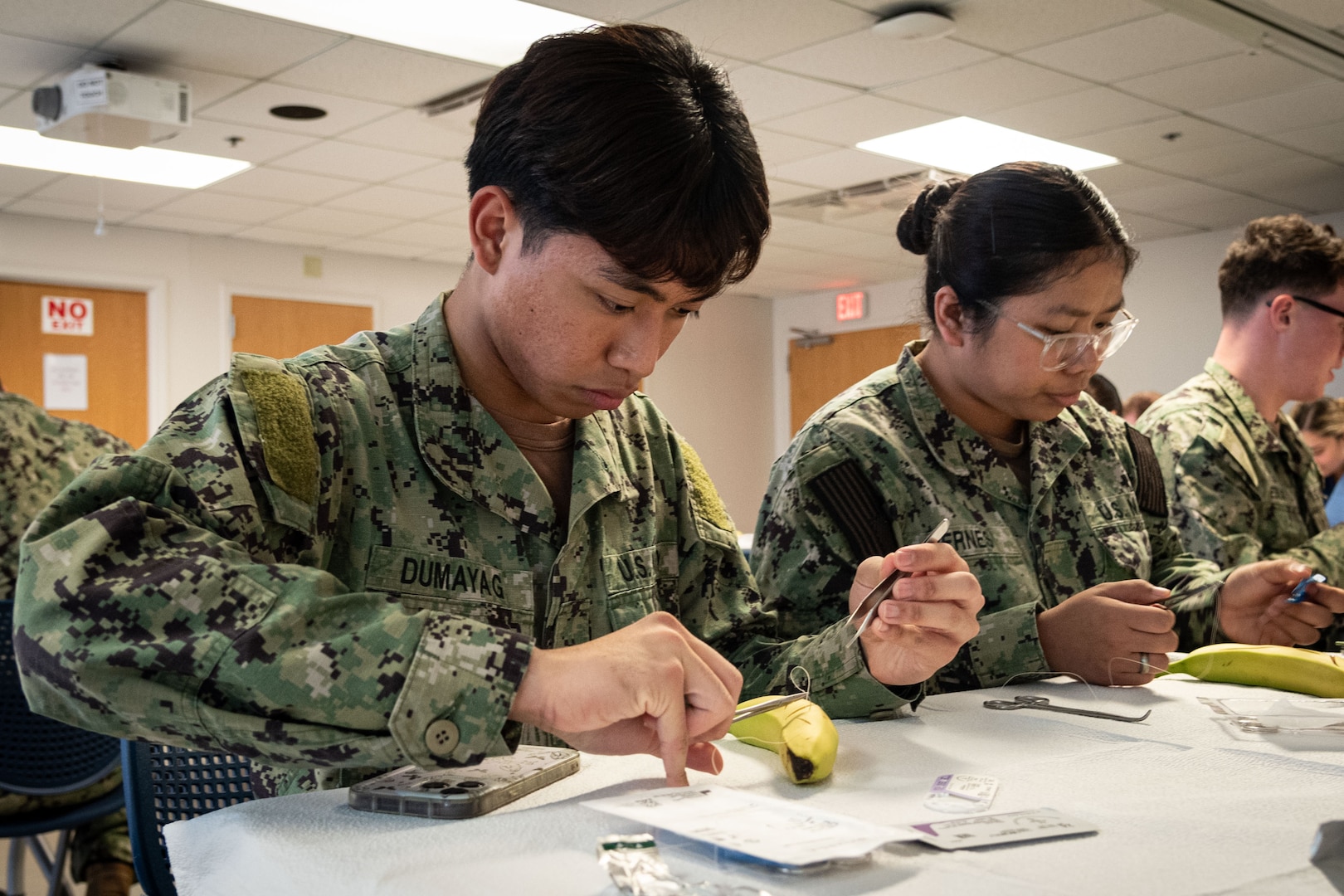 Hospitalman Marc Philip Dumayag, left, and Hospitalman MaAngeline Viernes, center, practice suturing techniques on bananas during a class held aboard Naval Health Clinic Cherry Point on Friday, November 15.  Bananas served as training aids for the class due to their thick and easy-to-pierce skin and the ability to distinguish the skin from the fruit.