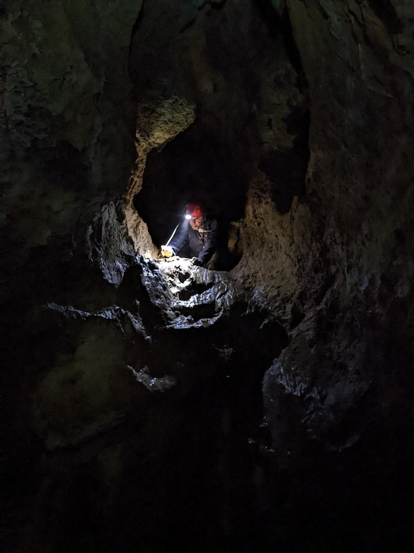 ERDC-CERL researcher, Aron Katz, in a cave wearing a helmet lamp, sampling for cave springtails in a drip pool, in El Capitan cave on Prince of Wales Island