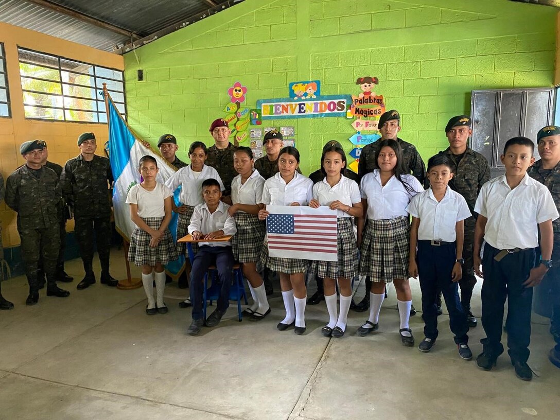 Students from Puerto Barrios, Guatemala, alongside members of the Guatemalan military display an American flag they crafted to show appreciation for the U.S. Army Civil Affairs team following a desk delivery to local schools, Oct. 25, 2024. This desk donation reflects the strong partnership between the U.S. military and partner nations throughout the Central American region. (U.S. Army courtesy photo)