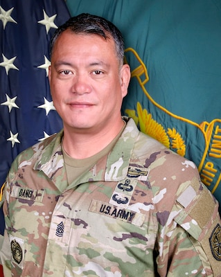 Man in U.S. Army uniform standing in front of two flags.