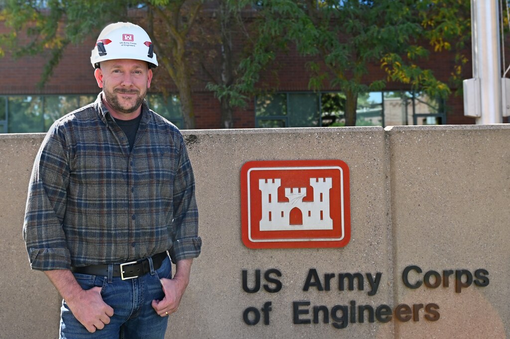 Ryan Laughery stands in front of the Walla Walla District sign at the District Headquarters building. He is wearing a hard hat.