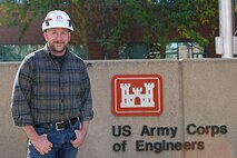 Ryan Laughery stands in front of the Walla Walla District sign at the District Headquarters building. He is wearing a hard hat.