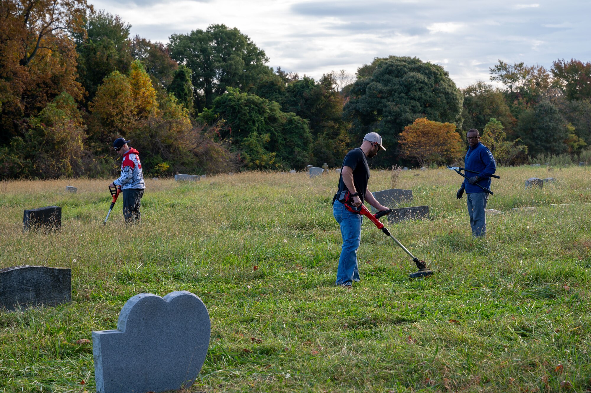 Three Airmen pictured cleaning up the vegetation at a graveyard.