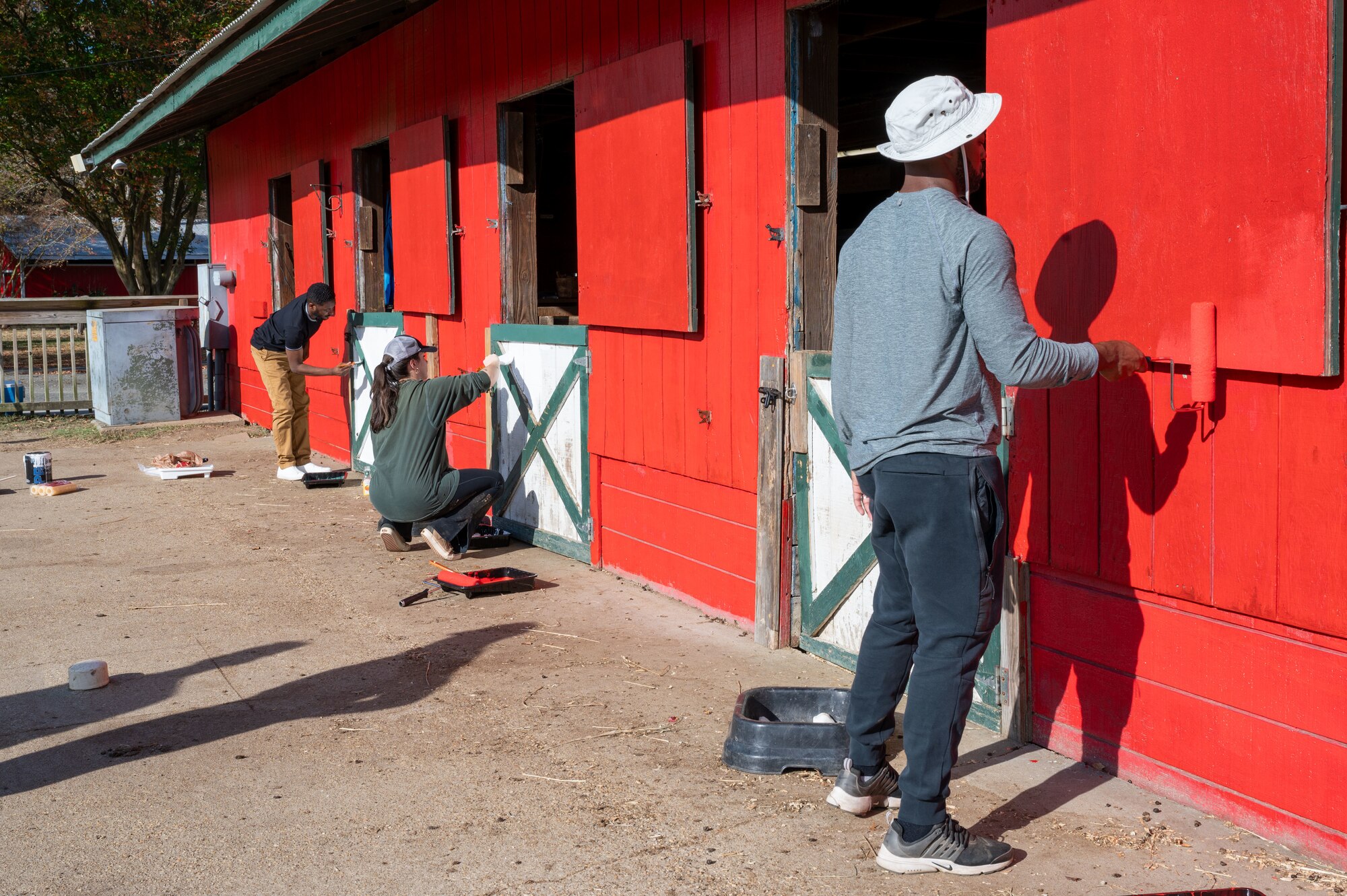 Multiple volunteers paint a red barn.