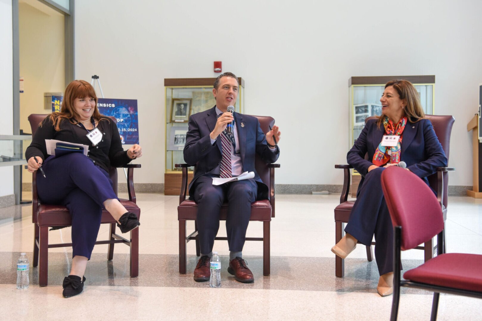 A man and two women sitting in chairs deliver remarks.