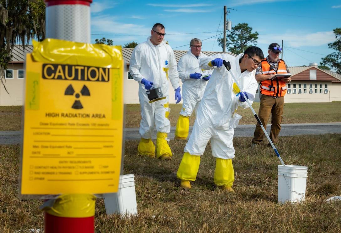 Men in hazardous material suits swab a field for radioactive material.