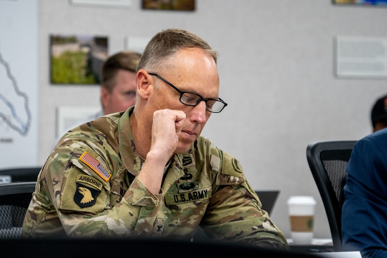 A man wearing a U.S. Army Uniform sits at a table during a meeting.