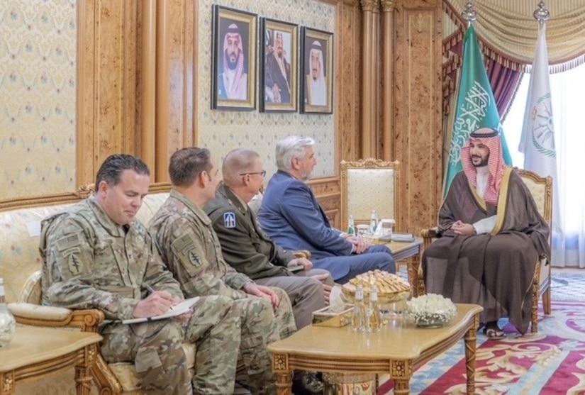 Four military officials sit next to a man in Middle Eastern attire.