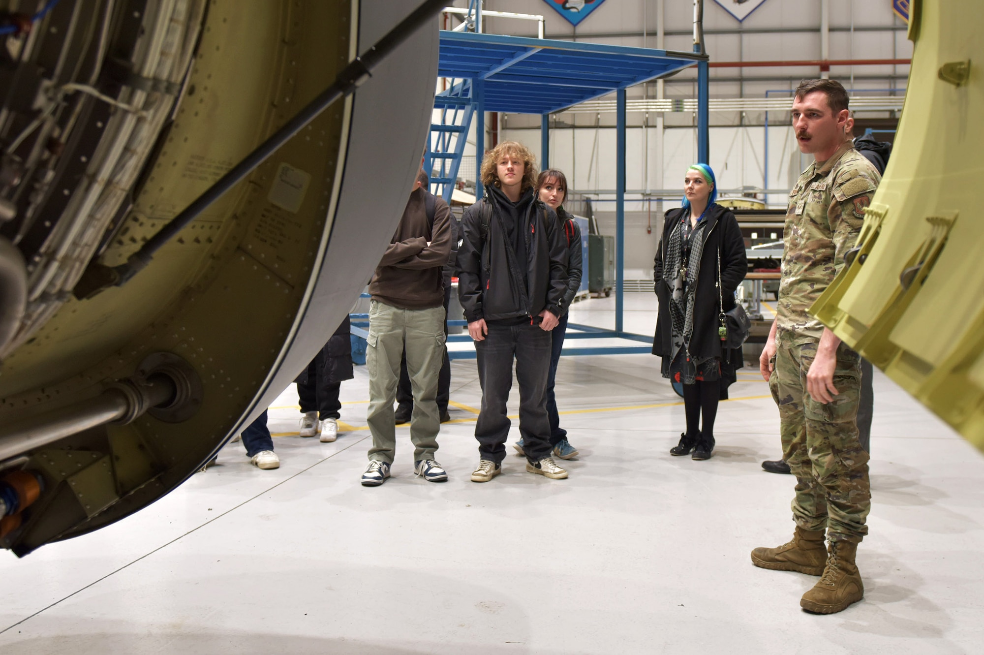 U.S. Air Force Senior Airman Logan Tubbs, right, 100th Maintenance Squadron crew chief, shows the engine of a KC-135 Stratotanker to a group of West Suffolk College engineering students during a tour at Royal Air Force Mildenhall, England, Nov. 15, 2024. The visit was arranged through the Honorary Commander program that pairs unit commanders with prominent members of the local community to enhance relationships between the base and civic leaders. (U.S. Air Force photo by Tech. Sgt. Chris Jacobs)